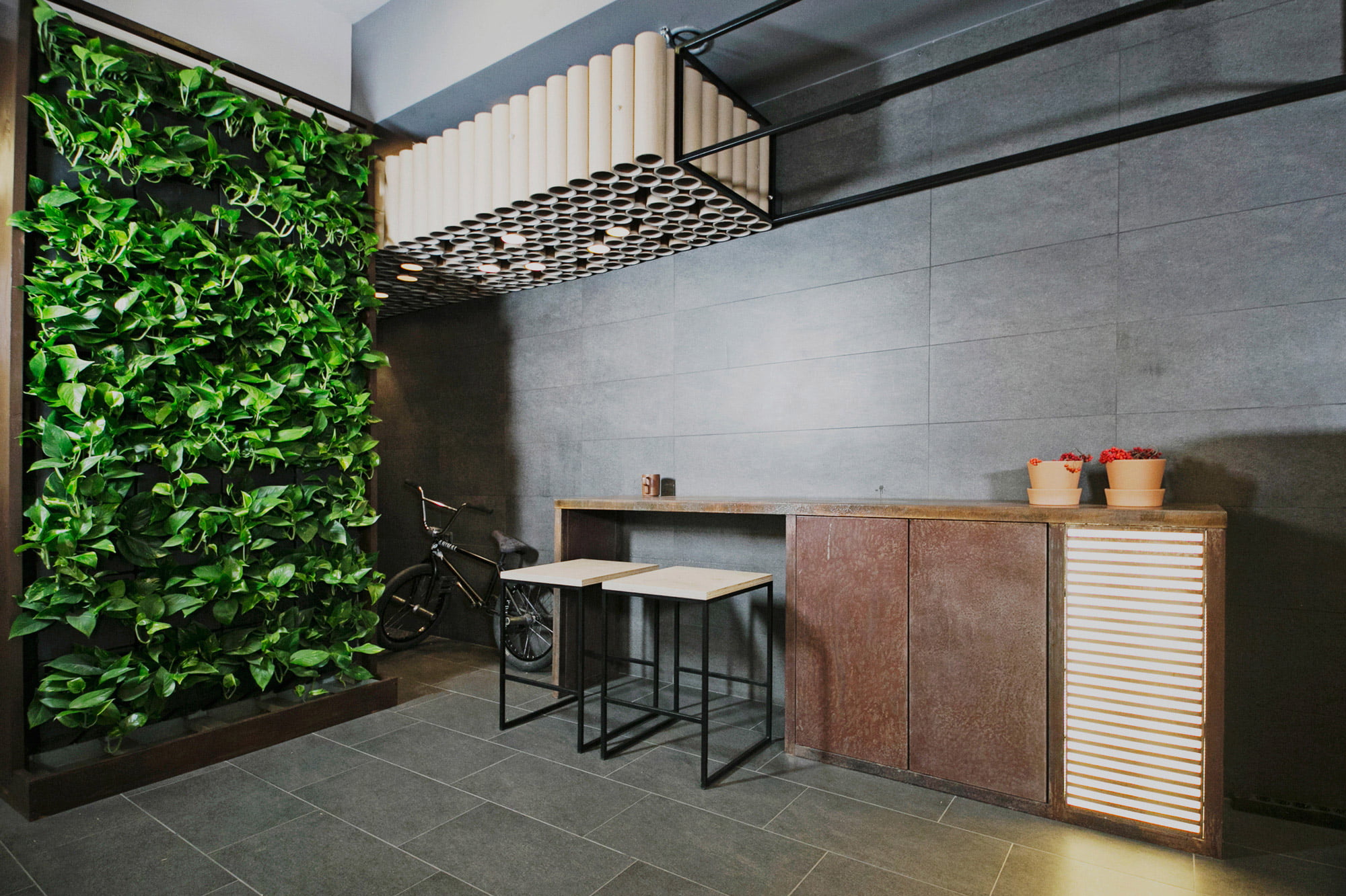 Eingangsbereich mit einer Efeuwand, einem BMX Bike, einem Tressen mit zwei Hockern und zwei Töpfen für Pflanzen