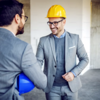 bauleitung Zwei Geschäftsmänner in Anzügen und mit Sicherheitshelmen auf einer Baustelle